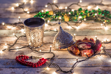 Dates, rosary, and water cup with Allah writing in arabic in lights background