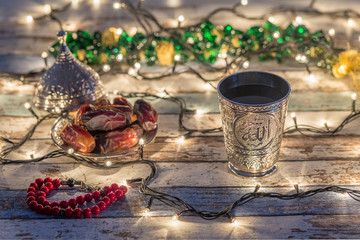 Dates, rosary, and water cup with Allah writing in arabic in lights background