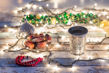 Dates, rosary, and water cup with Allah writing in arabic in lights background