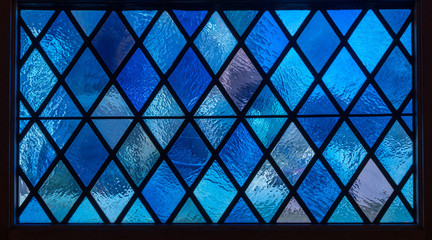 Detail of blue diamond shaped panes in colored light from stained glass window in catholic church - obrazy, fototapety, plakaty