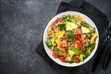 Quinoa salad with fresh vegetables on black.