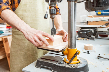 Close-up of a joiner hands working with wood on a lathe drilling machine at the factory. Carpenter...