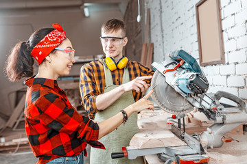 A male craftsman explains to a girl apprentice how to work with an automated saw machine in a factory or workshop
