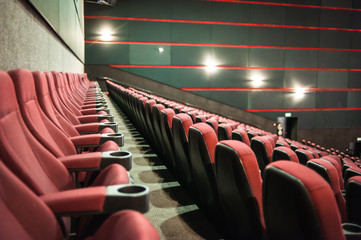 Empty cinema. Rows of comfortable red chairs towards to big screen in illuminate red room cinema. Mock Up.