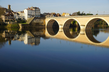 Fototapeta premium mirror reflection of an old stone bridge and buildings in the river at dusk