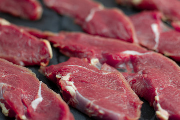 Red pieces of fresh veal, sliced into raw thin beef steaks, laid out on a wooden board. Raw beef for steaks with streaks of fat.