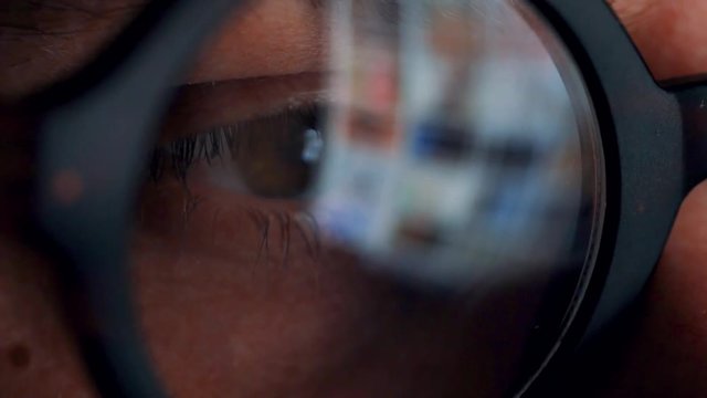 Man in glasses looking on the monitor and surfing Internet. The monitor screen is reflected in the glasses