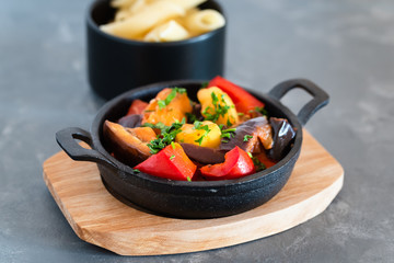 Vegetarian ratatouille with baked aubergine, zucchini, pepper in tomato sauce. Dish served with pasta.