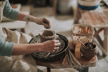 Young woman cutting off clay with string while working on pottery wheel