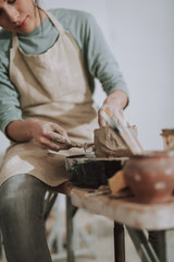 Obraz na płótnie Canvas Young lady using sculpture scraper knife while making clay pot