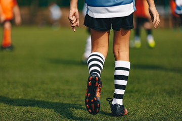 Plakat Legs of boy footballer in boots football cleats. Player walking on green grass soccer field at the stadium. Close-up of football sports equipment