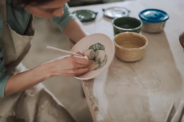 Foto op Plexiglas Young lady in apron painting ceramic plate at workshop © Yakobchuk Olena