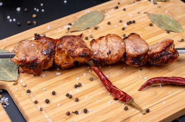 cooked barbecue on a skewer is on the Board sprinkled with chili pepper, black pepper and salt