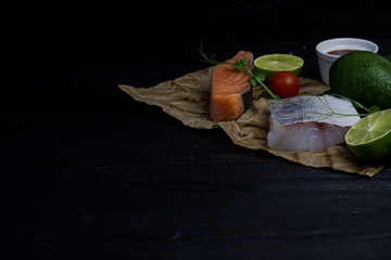 salmon and pike-perch steak with lime on wooden dark background with ripe avocado