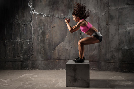 Fit young woman box jumping at a crossfit style on gray background. Fitness, crossfit, functional, training, and lifestyle concept