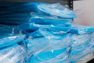 A variety of disposable medical blue garments in bags on the shelves. Factory disposable clothing.