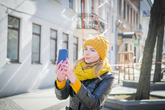 Beautiful woman in a yellow knitted hat takes pictures of herself on her mobile phone