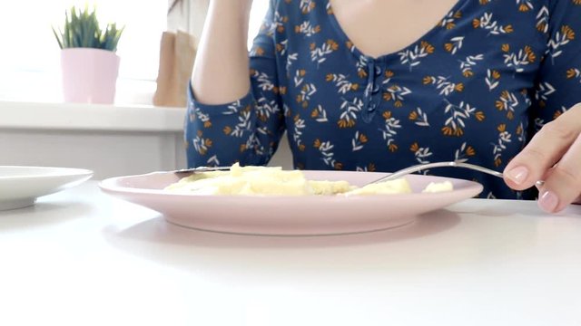 Woman sitting by the table, eating an omlet with a folk and a knife and drinking coffee or tea for breakfast at home or restaurant