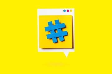 Paper cutout of hashtag symbol on a yellow speech bubble on yellow background. Concept of social media and digital marketing.