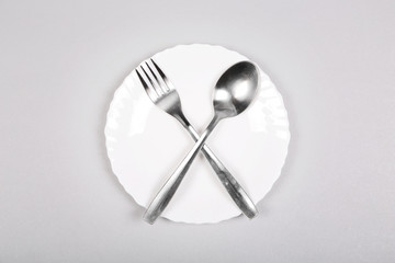 Fork and spoon on an empty white plate on gray background. 