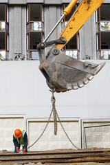 Excavator bucket lifting metal beam with worker helping, construction site and demolished building...