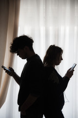 Silhouette of two teenagers with cell phones standing back to back - 258614058