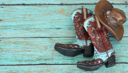 cowboy boots and hat laying on a teal background