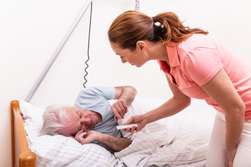 Pflegerin in Alten Pflegeheim gibt älterem Mann im Bett Medizin Medikament 