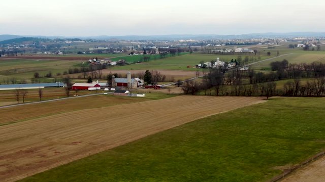 Aerial pan of a red farmhouse, barn, silos, and other buildings surrounded by harvested brown and green fields Lancaster County, Pennsylvania. Concept: farm life, Amish, rural