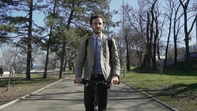 Young business man in suit, tie and backpack riding on  electric scooter,modern office worker ride on scooter outdoors