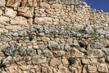 Background of ancient Greek rock wall with vegetation and moss growing between some rocks and a corner of blue sky showing