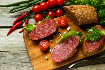 Sandwiches with sausage, tomatoes, onions on a cutting board.