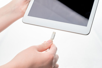 girl's hands stick the charger into the tablet on a white background close-up