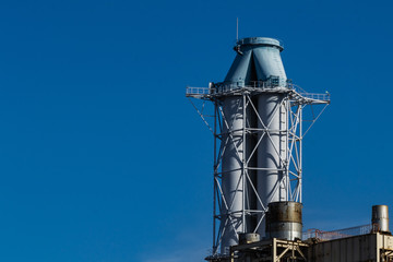 It is a chimney of a thermal power plant that rises in the blue sky.