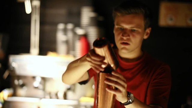 Skilled attractive bartender pouring an alcoholic drink into a glass with ice cubes on the bar counter. Party with friends in trendy pub.