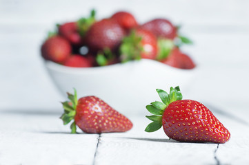 Fresh ripe organic strawberry fruit in white bowl on white wooden background, close up harvested strawberries concept