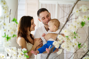 Obraz premium Loving parents affectionately cradling adorable baby son in their arms looking at him. Childhood, parenthood, togetherness, love, happiness concept