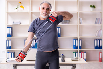White bearded old man employee doing exercises in the office 