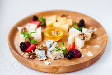 Tasty appetizer. Plate of cheese. banquet, restaurant menu. slices of various cheeses. camembert, parmesan, dorblu and maasdam served with fruits, walnuts and honey on wooden board