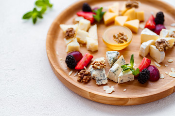 cheese plate, delicious appetizer to wine with fruits, nuts, honey, served on a light wooden board. camembert, parmesan, dorblu and maasdam  slices, gourmet food, banquet