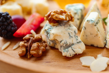 blue cheese, dorblu slices close up. cheeseboard served with fruits, walnuts and honey. delicious snack on wooden platter