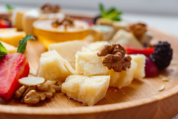 Cheese plate. slices of parmesan, dorblu, camembert and maasdam served with walnuts and honey on wooden board