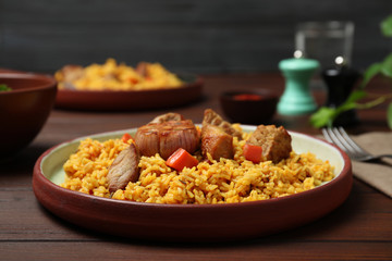 Plate with rice pilaf and meat on wooden table