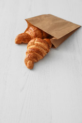 Paper bag with pastry on light wooden background. Space for text