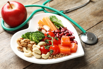Plate with products for heart-healthy diet, apple and stethoscope on wooden background