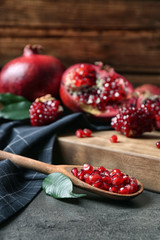 Ripe pomegranates and spoon with seeds on table against wooden background