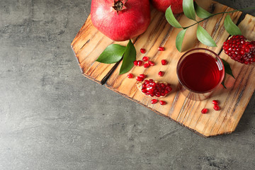 Board with glass of pomegranate juice and fresh fruits on grey background, top view. Space for text