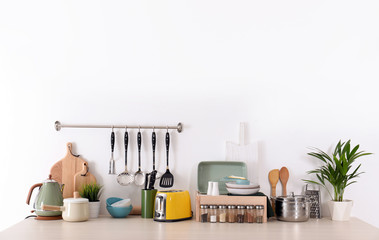 Set of clean cookware, dishes, utensils and appliances on table at white wall