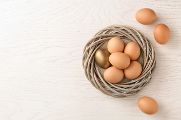 Golden egg among others in nest on wooden background, top view with space for text