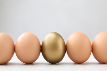 Golden egg among others on white table